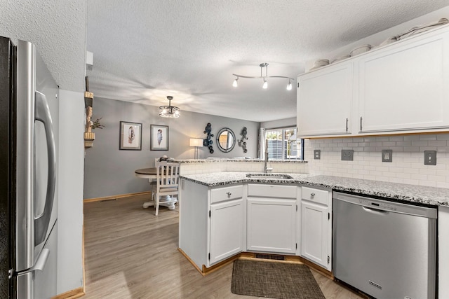 kitchen with stainless steel appliances, sink, white cabinets, kitchen peninsula, and light hardwood / wood-style flooring