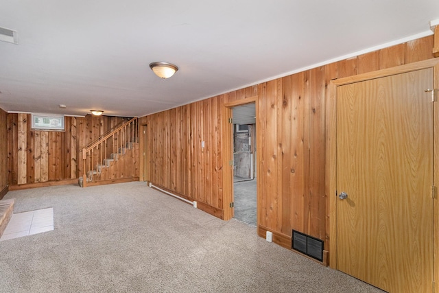 basement with wooden walls, light colored carpet, and a baseboard heating unit