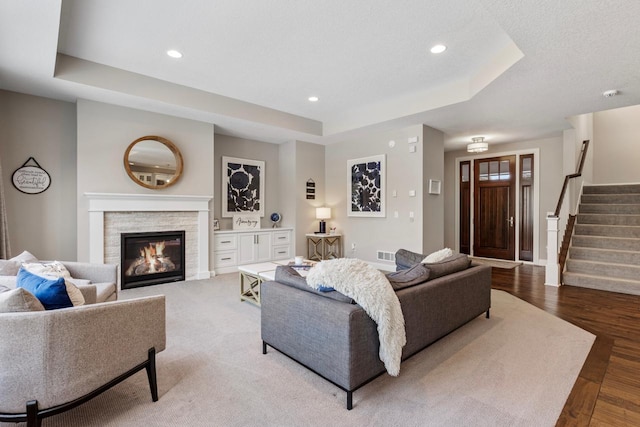 living room with hardwood / wood-style floors, a raised ceiling, and a stone fireplace