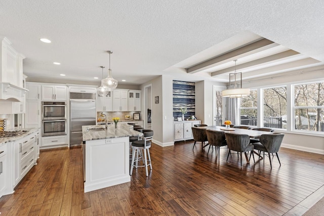 kitchen with decorative backsplash, appliances with stainless steel finishes, an island with sink, white cabinets, and light stone counters