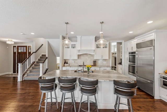 kitchen featuring white cabinetry, an island with sink, stainless steel appliances, dark hardwood / wood-style flooring, and pendant lighting