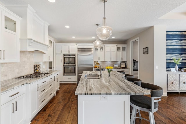 kitchen featuring pendant lighting, white cabinets, stainless steel appliances, sink, and a center island with sink