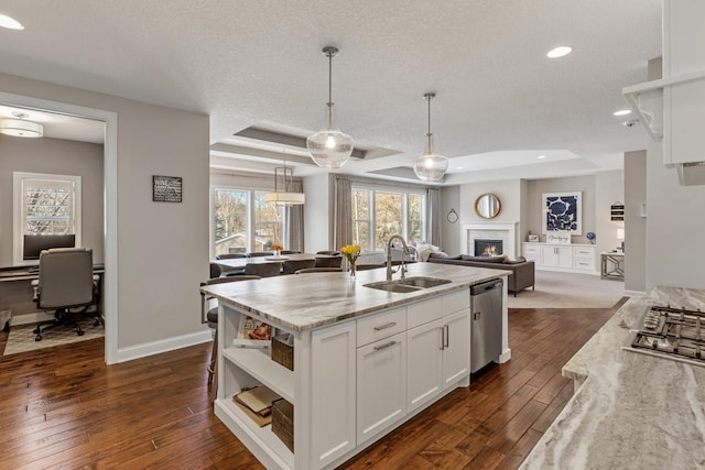 kitchen with pendant lighting, white cabinetry, sink, light stone counters, and a tray ceiling