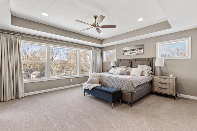 carpeted bedroom with a textured ceiling, ceiling fan, and a tray ceiling