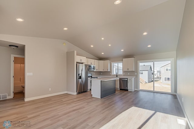 kitchen with white cabinetry, appliances with stainless steel finishes, a center island, light wood-type flooring, and vaulted ceiling