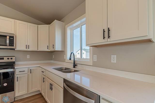 kitchen with white cabinetry, appliances with stainless steel finishes, sink, hardwood / wood-style flooring, and vaulted ceiling