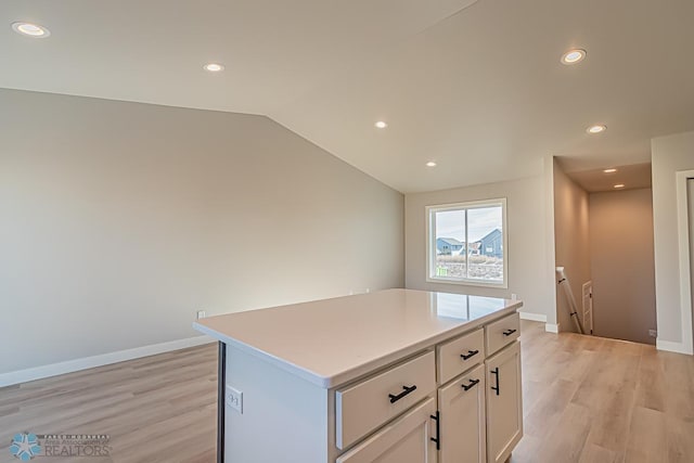 kitchen featuring a kitchen island, light wood-type flooring, lofted ceiling, and white cabinets