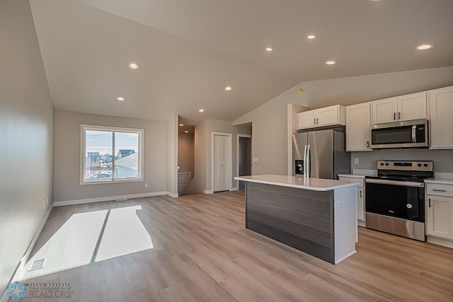 kitchen with vaulted ceiling, white cabinets, a kitchen island, light wood-type flooring, and appliances with stainless steel finishes