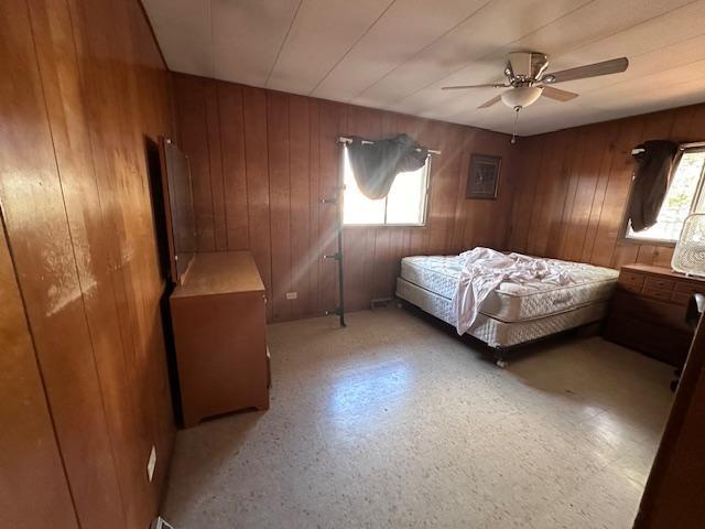 bedroom with ceiling fan, multiple windows, and wooden walls