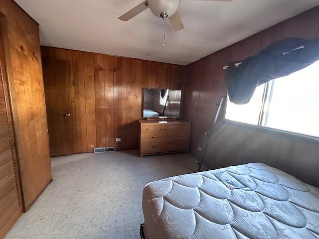 bedroom with a closet, wooden walls, and ceiling fan