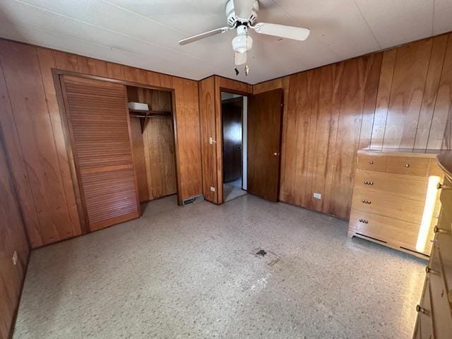 unfurnished bedroom featuring wood walls, ceiling fan, and a closet