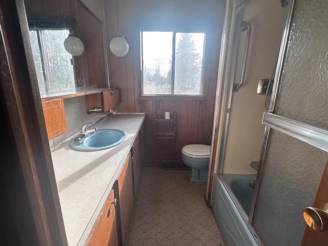 full bathroom with toilet, vanity, wooden walls, and enclosed tub / shower combo