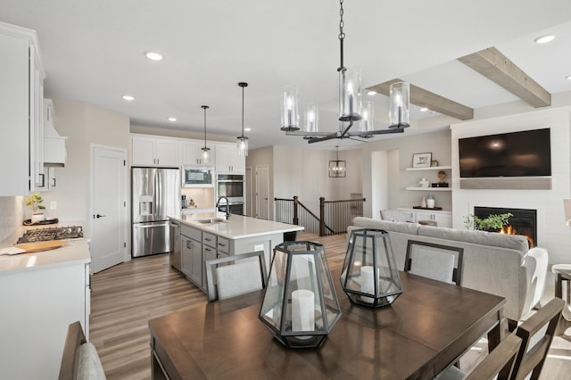 dining area with a large fireplace, wood-type flooring, beamed ceiling, and sink