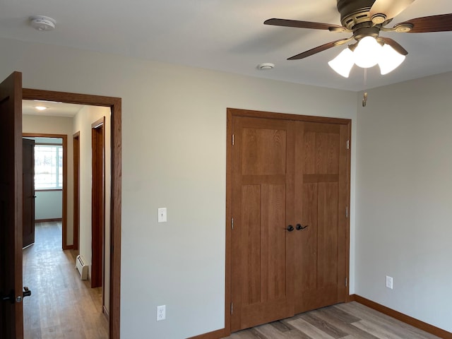 unfurnished bedroom with ceiling fan, a baseboard heating unit, light wood-type flooring, and a closet