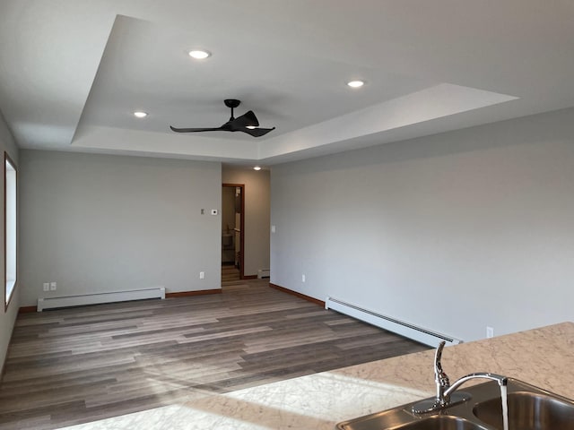 empty room featuring wood-type flooring, a tray ceiling, baseboard heating, and ceiling fan