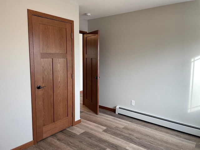 unfurnished bedroom featuring light wood-type flooring and a baseboard heating unit