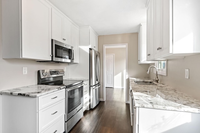 kitchen with light stone countertops, dark wood finished floors, a sink, appliances with stainless steel finishes, and white cabinetry