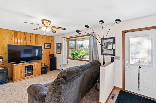 carpeted living room with wooden walls, plenty of natural light, and ceiling fan