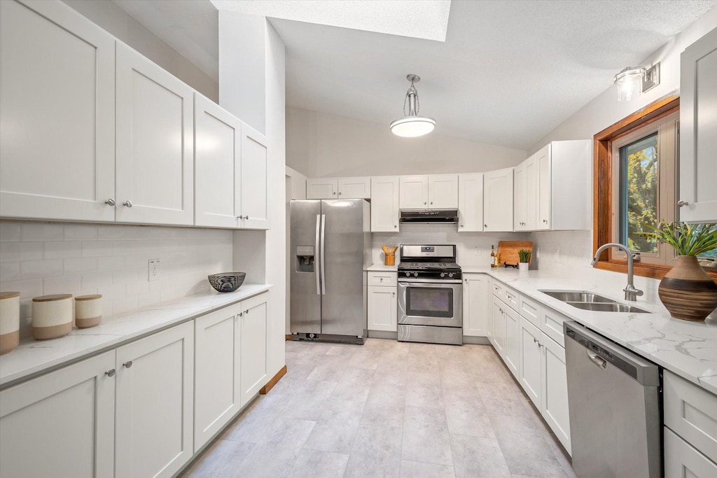 kitchen featuring light stone counters, stainless steel appliances, vaulted ceiling, sink, and white cabinetry