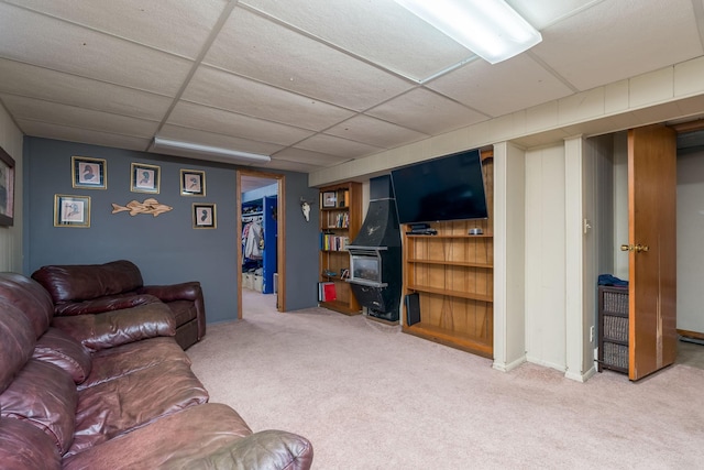 living room with a wood stove, light carpet, and a drop ceiling