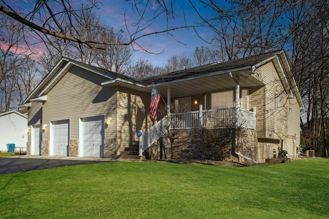 view of front of property with covered porch, central air condition unit, a garage, and a lawn