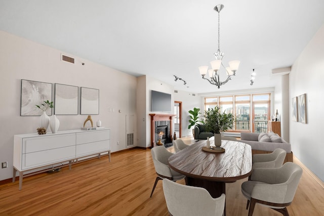 dining room with a chandelier, light wood-type flooring, a glass covered fireplace, and track lighting