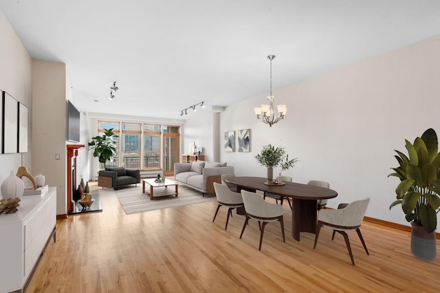 dining space featuring baseboards, light wood finished floors, rail lighting, and a notable chandelier