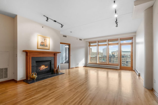 unfurnished living room with a glass covered fireplace, a city view, baseboard heating, and wood finished floors