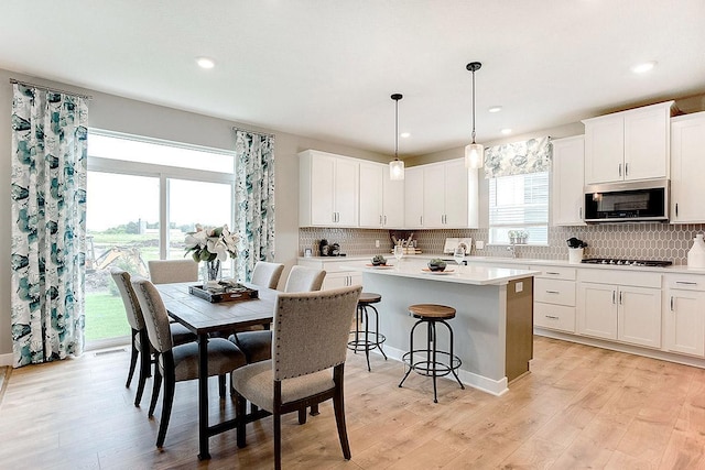 kitchen with stainless steel appliances, white cabinetry, decorative light fixtures, a kitchen island, and decorative backsplash