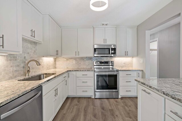 kitchen with stainless steel appliances, backsplash, sink, white cabinets, and light hardwood / wood-style flooring