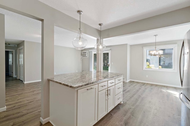 kitchen with light stone counters, white cabinets, a textured ceiling, stainless steel refrigerator, and light wood-type flooring