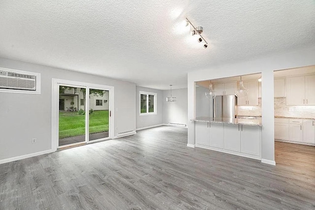 unfurnished living room featuring hardwood / wood-style floors, a textured ceiling, track lighting, and a wall mounted air conditioner