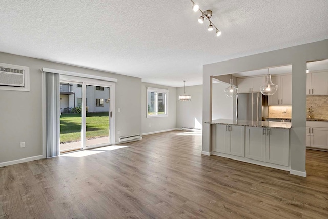 unfurnished living room featuring dark hardwood / wood-style flooring, a wall unit AC, a textured ceiling, and baseboard heating