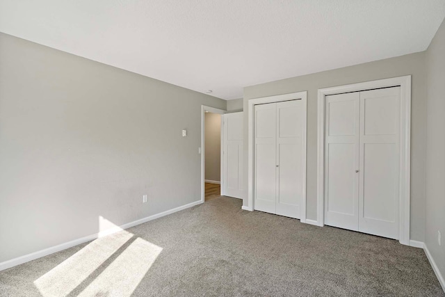 unfurnished bedroom featuring light carpet and two closets