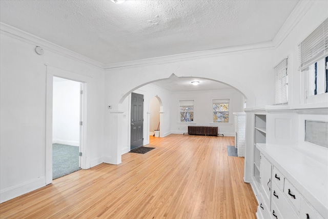 unfurnished living room with a textured ceiling, crown molding, light wood-type flooring, and radiator