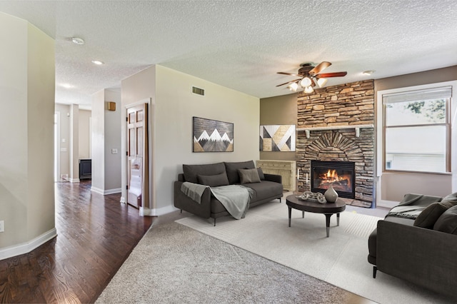 living room featuring a fireplace, a textured ceiling, dark hardwood / wood-style flooring, and ceiling fan