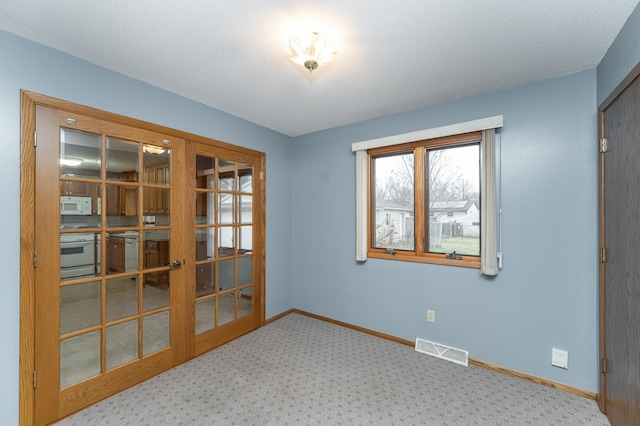 carpeted spare room with french doors and a textured ceiling