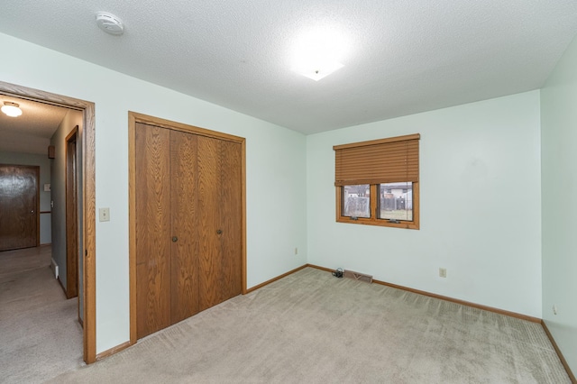 unfurnished bedroom with a textured ceiling, light colored carpet, and a closet