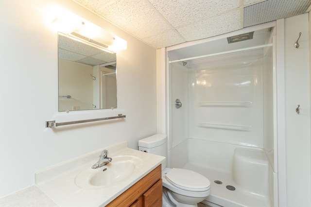 bathroom featuring a paneled ceiling, toilet, vanity, and walk in shower