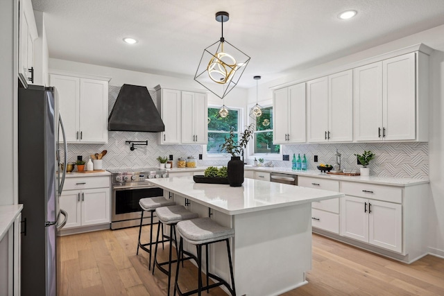 kitchen with light hardwood / wood-style floors, custom exhaust hood, a kitchen island, white cabinetry, and appliances with stainless steel finishes