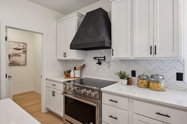 kitchen with premium range hood, backsplash, light hardwood / wood-style floors, white cabinets, and stainless steel range oven