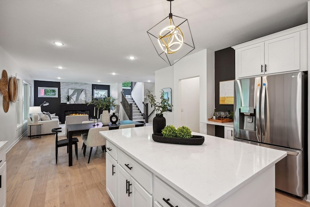 kitchen with white cabinetry, stainless steel refrigerator with ice dispenser, hanging light fixtures, light hardwood / wood-style flooring, and a kitchen island