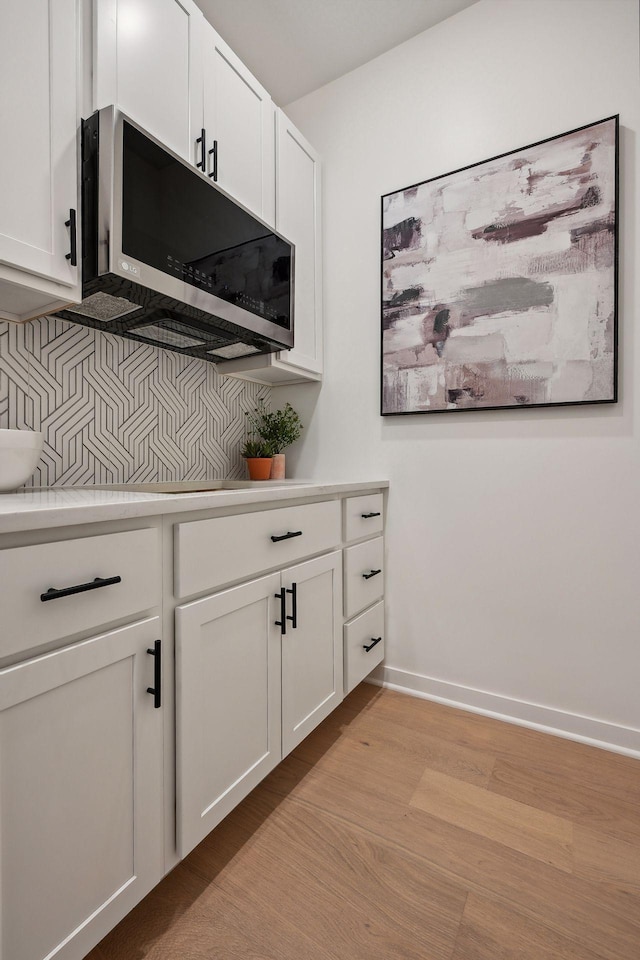 kitchen with tasteful backsplash, white cabinetry, and light wood-type flooring