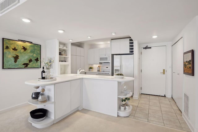 kitchen featuring kitchen peninsula, white appliances, sink, light tile patterned floors, and white cabinetry