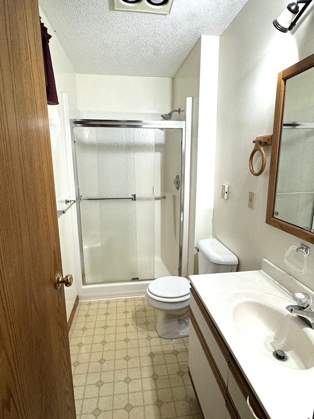 bathroom featuring a textured ceiling, vanity, an enclosed shower, and toilet