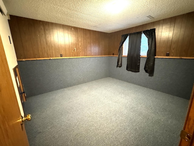 carpeted empty room with wood walls and a textured ceiling