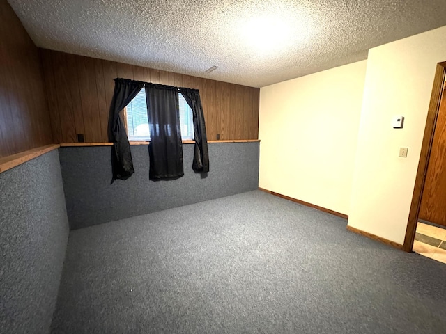 carpeted spare room featuring wood walls and a textured ceiling