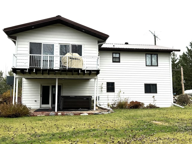 rear view of house with a lawn, a balcony, and a hot tub