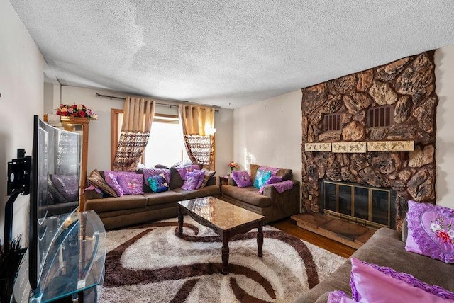 living room featuring hardwood / wood-style floors, a stone fireplace, and a textured ceiling