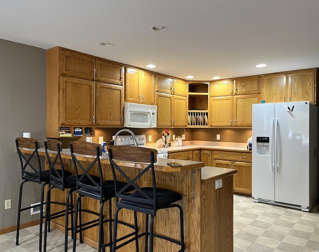 kitchen with kitchen peninsula, white appliances, and a kitchen breakfast bar